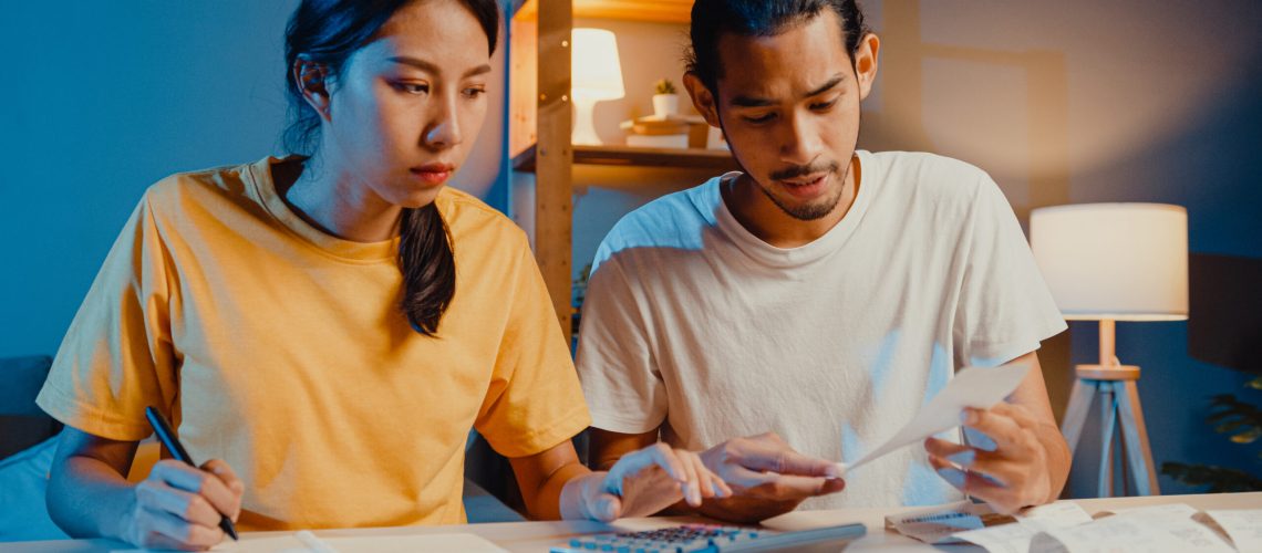 Stress asia couple man and woman use calculator for calculate family budget, debts, expenses during financial economic crisis at home at night. Marriage money trouble, Family budget plan concept.